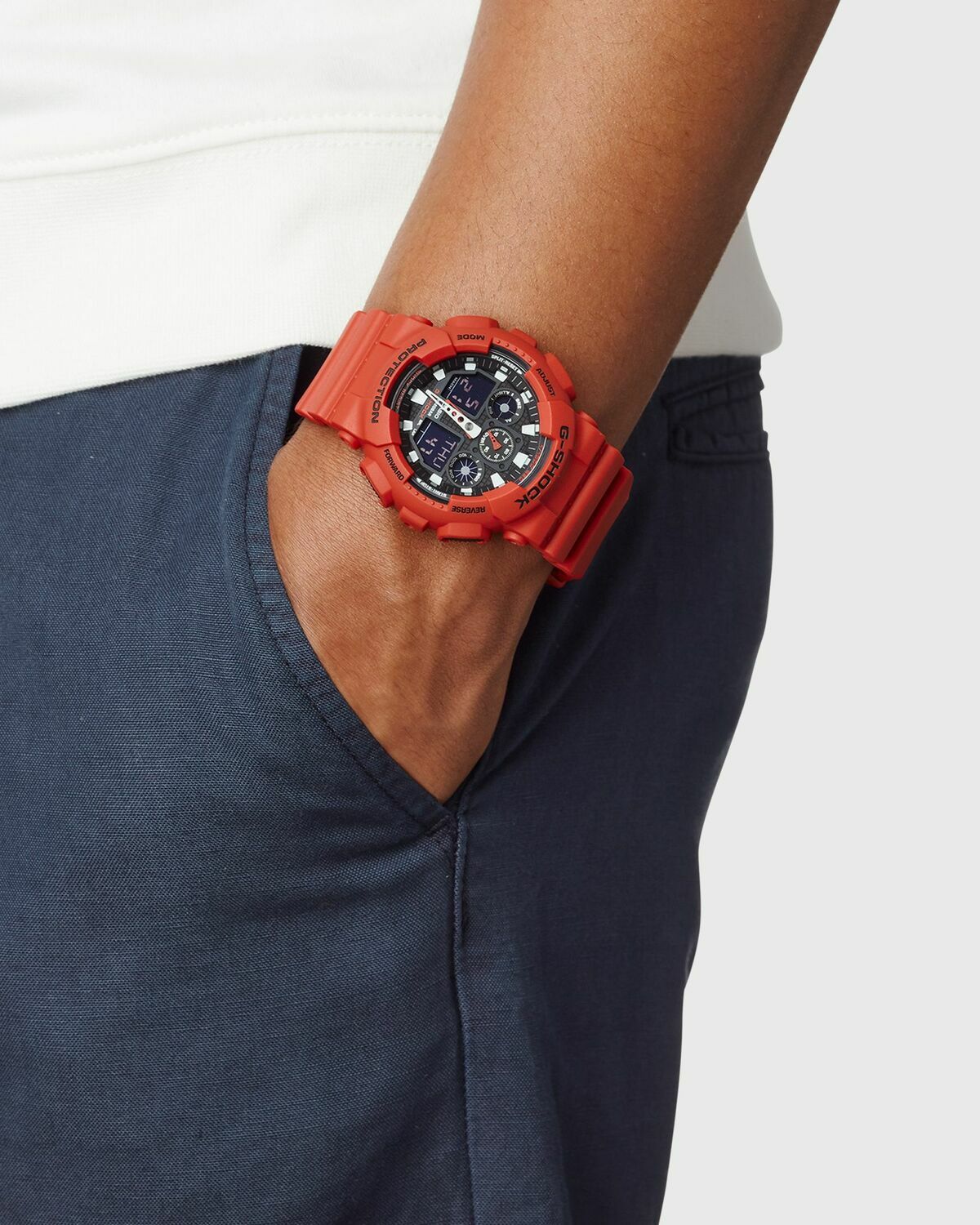 Đồng hồ G-Shock GA-100 màu đỏ đeo trên cổ tay cùng trang phục năng động.