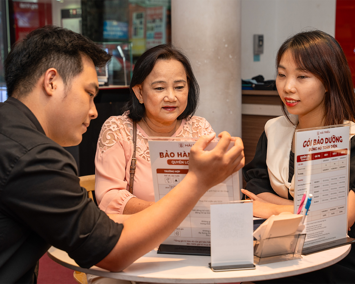 Nhân viên tại Đồng Hồ Hải Triều đang tư vấn và giải thích chi tiết bảng quyền lợi gói bảo dưỡng, chính sách bảo hành lên đến 5 năm cho khách hàng.