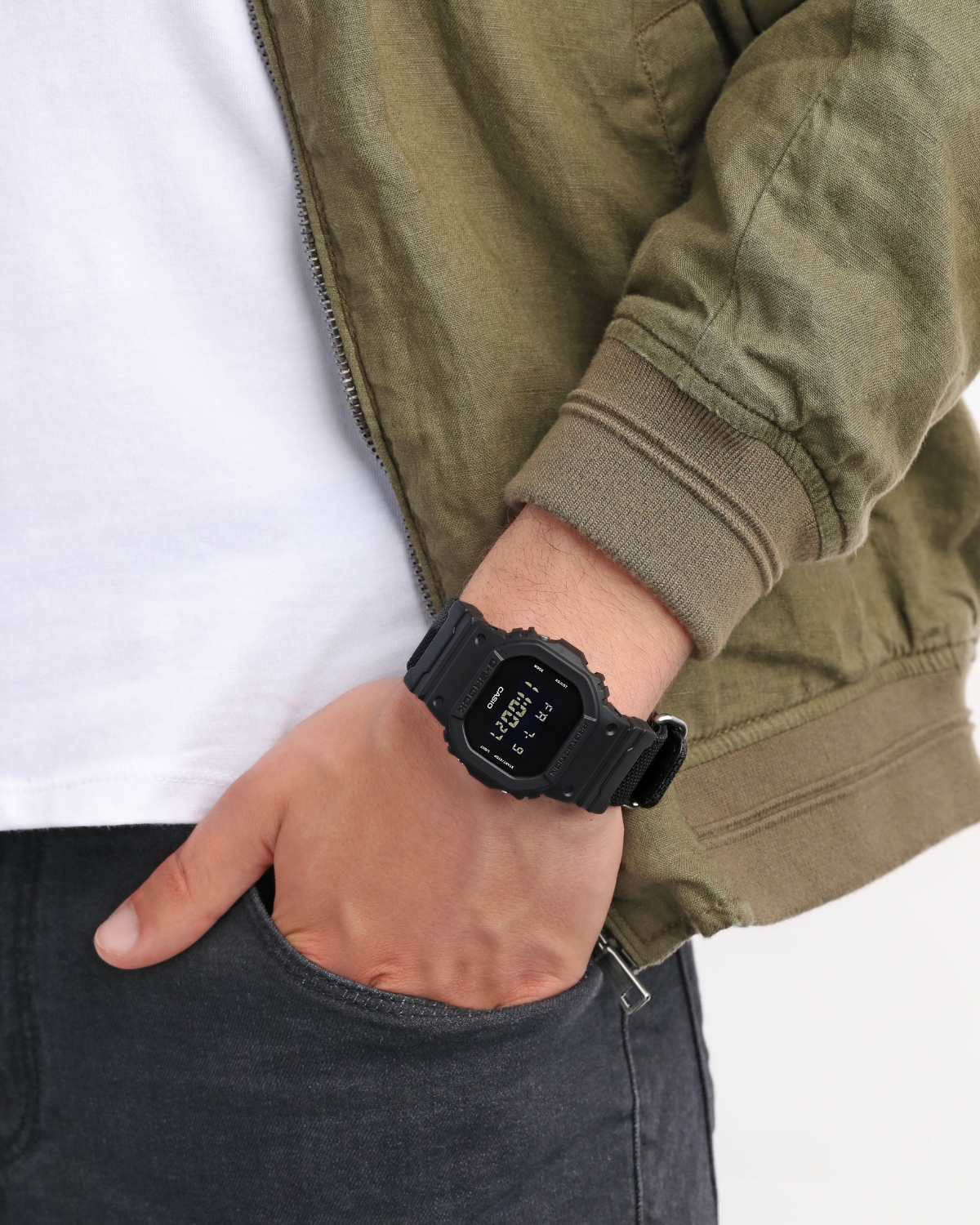 Đồng hồ G-Shock DW-5600BBN-1DR dây vải đen đeo trên cổ tay, phối cùng áo khoác xanh phong cách streetwear.