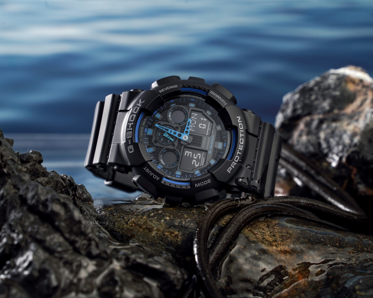 Đồng hồ G-Shock GA-100-1A2NDR phối xanh đặt trên đá cạnh mặt nước.