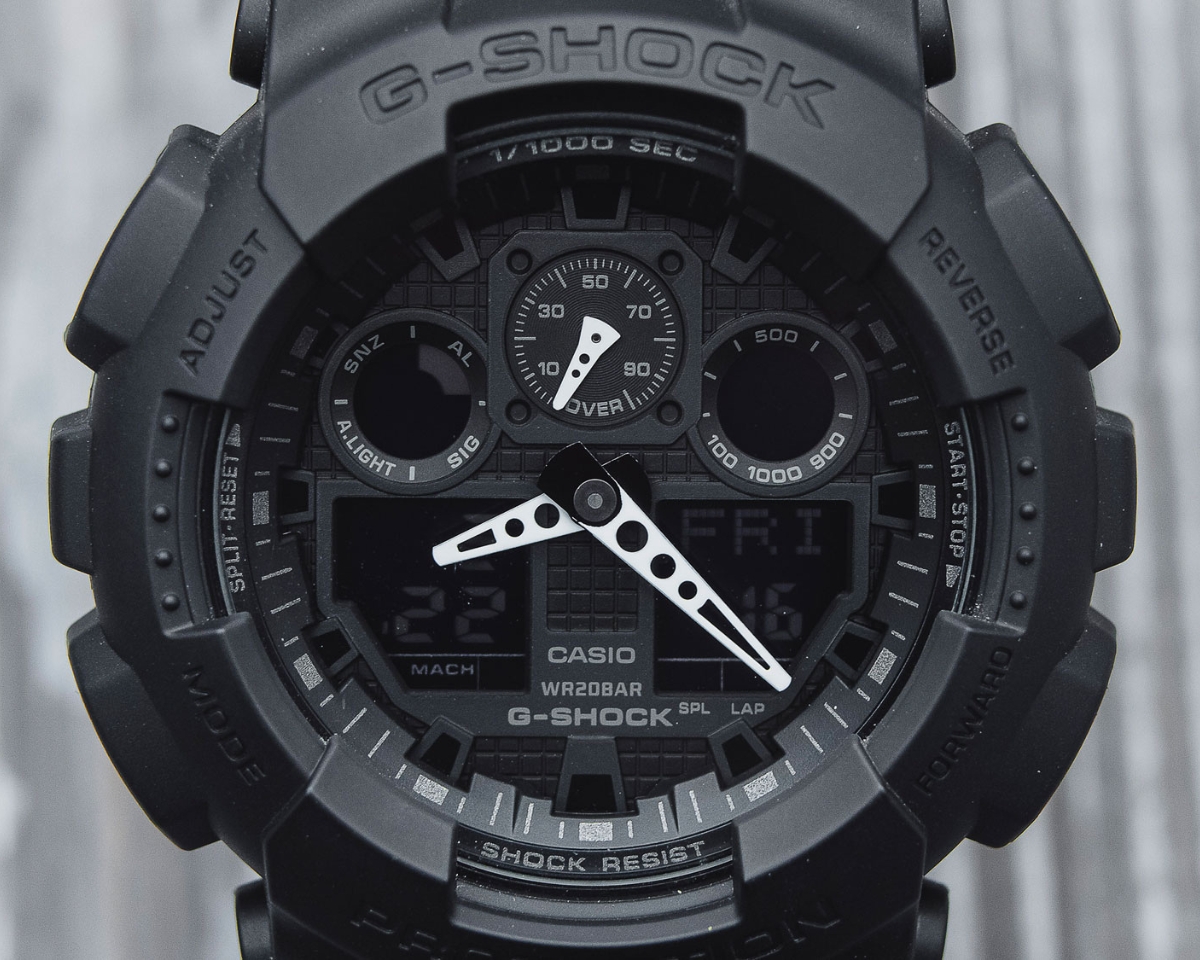 Cận cảnh mặt số G-Shock GA-100 all-black với kim trắng và màn hình điện tử.