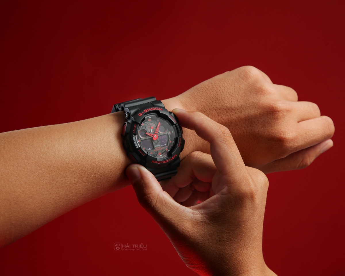 Người dùng chỉnh nút trên đồng hồ G-Shock GA-100 đen đỏ khi đeo trên tay.