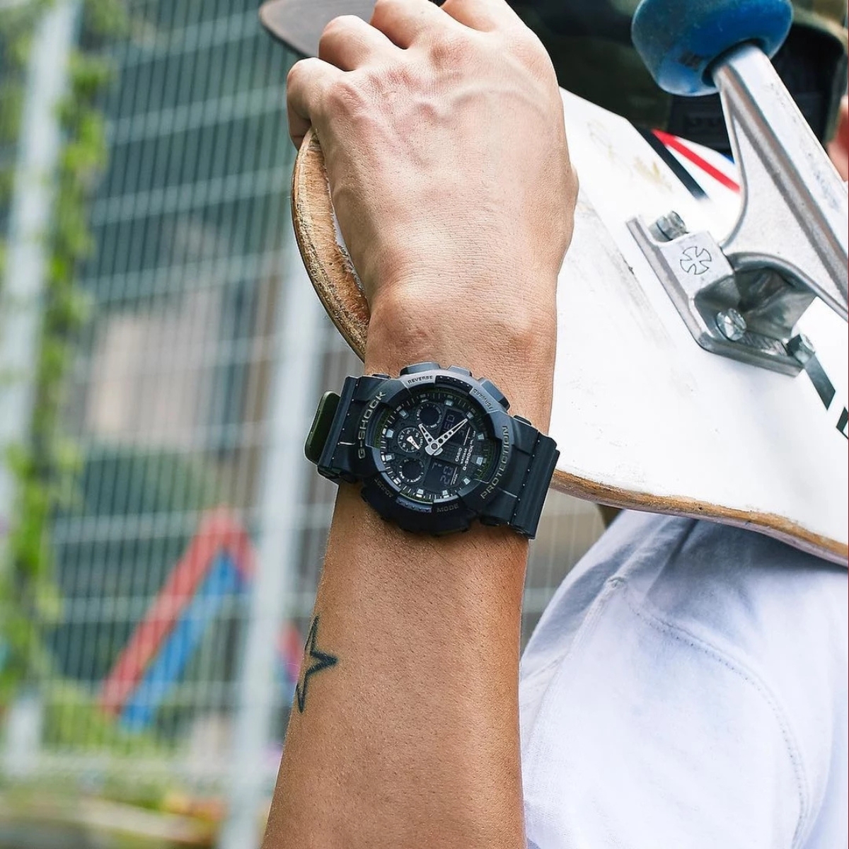 Đồng hồ G-Shock GA-100 đen đeo khi cầm ván trượt ngoài trời.