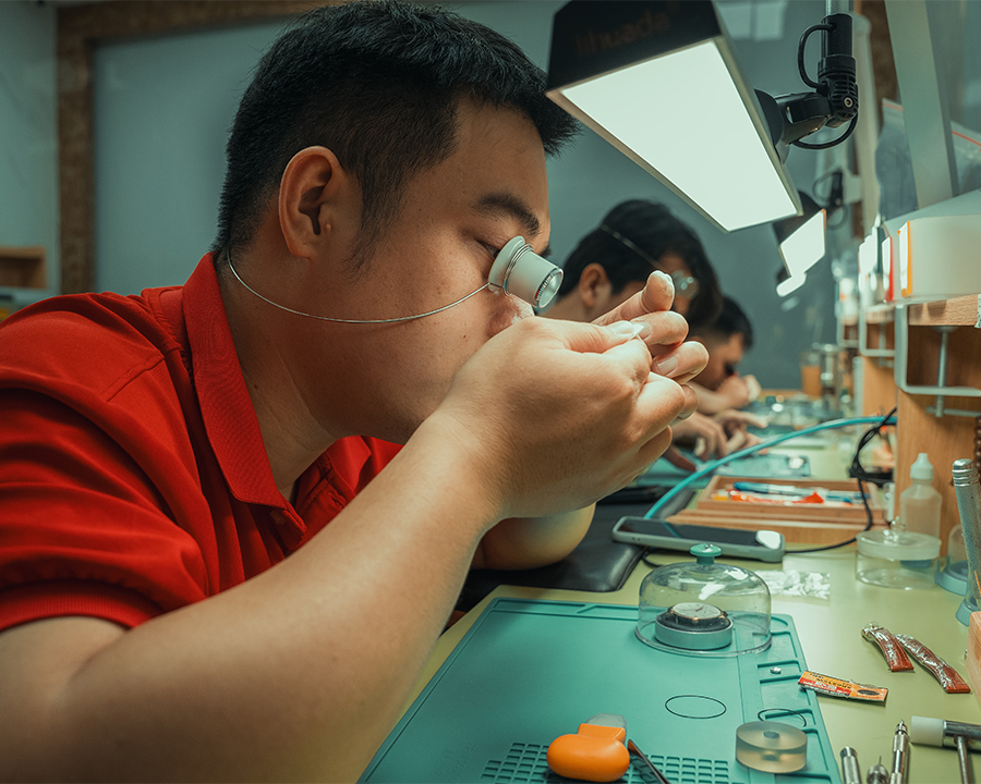 Kỹ thuật viên đeo kính lúp chuyên dụng đang tập trung sửa chữa và kiểm tra linh kiện đồng hồ.