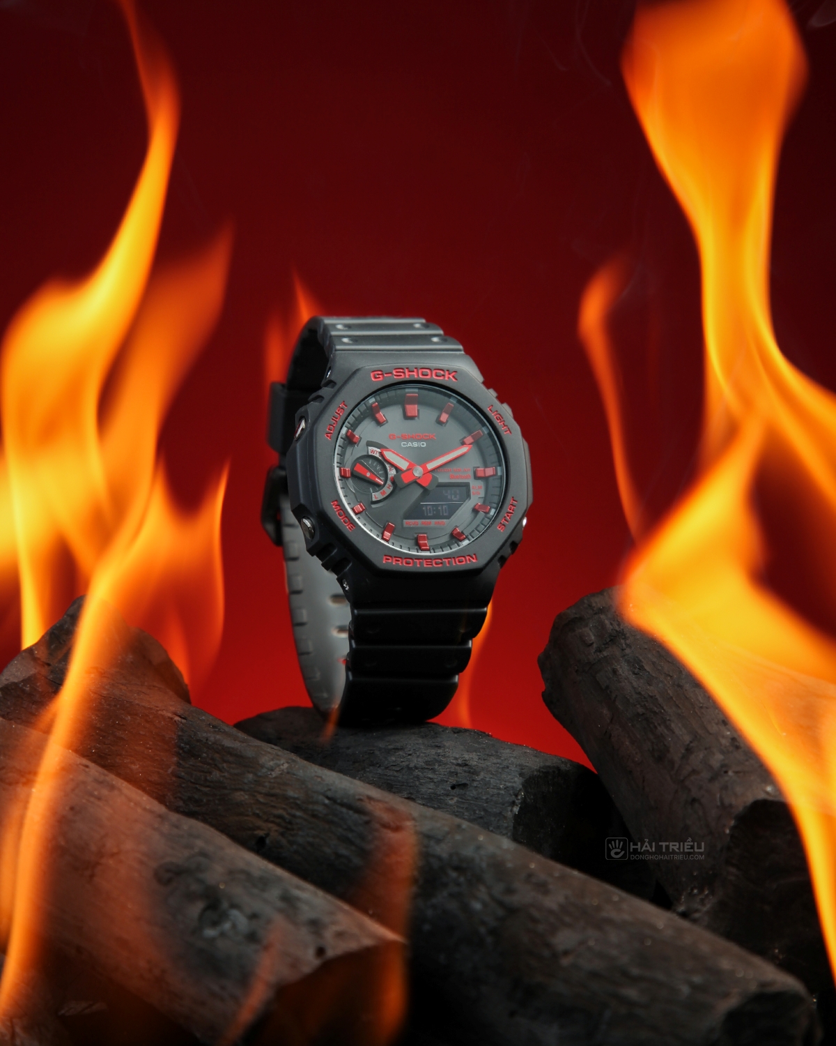 Đồng hồ G-Shock GA-B2100BNR-1ADR phối đỏ đen đặt giữa than và lửa, thể hiện phong cách thể thao mạnh mẽ.