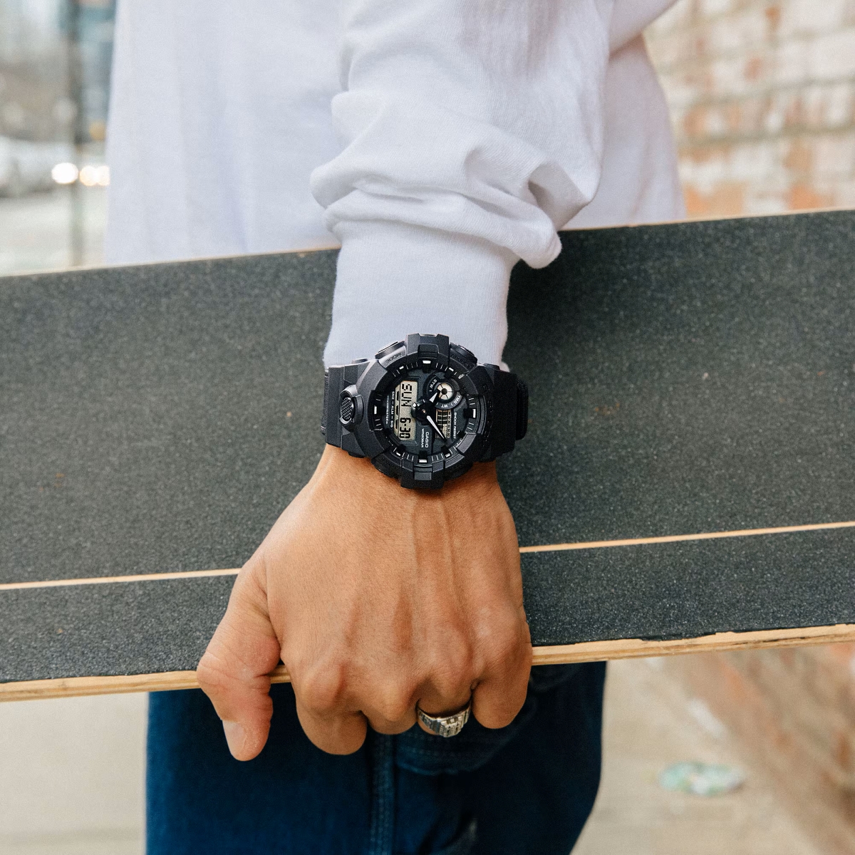 G-Shock GA-700 màu đen đeo trên cổ tay khi cầm ván trượt, phù hợp phong cách năng động.