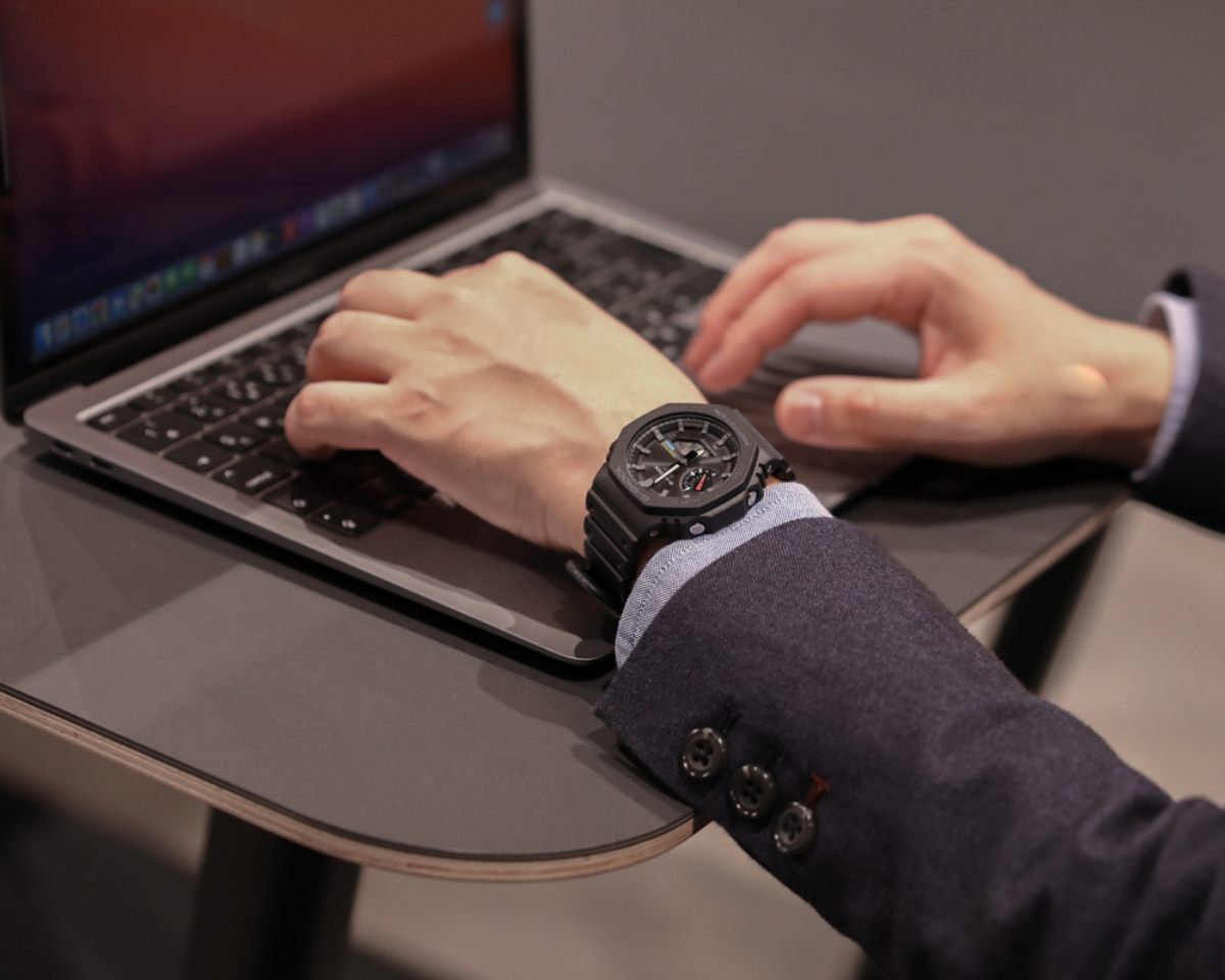 Đồng hồ G-Shock GA-B2100 màu đen trên cổ tay người dùng khi làm việc với laptop.