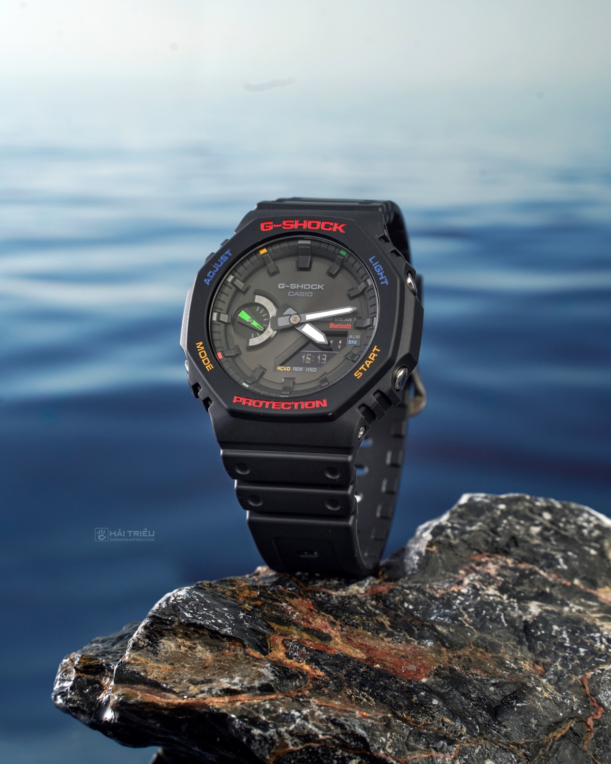 Đồng hồ G-Shock GA-B2100 màu đen phối chi tiết đa sắc đặt trên đá, nổi bật với phong cách thể thao bền bỉ.