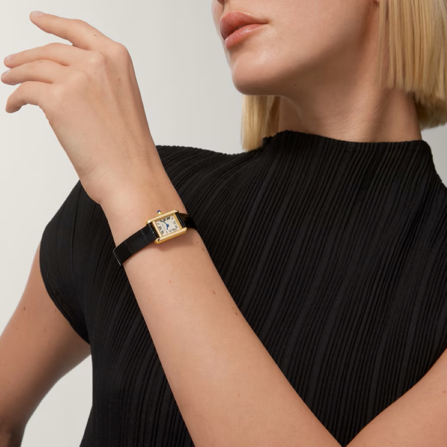 Người mẫu đeo chiếc đồng hồ nữ Cartier Tank vỏ vàng, mặt số chữ nhật cổ điển kết hợp cùng dây da trên cổ tay.