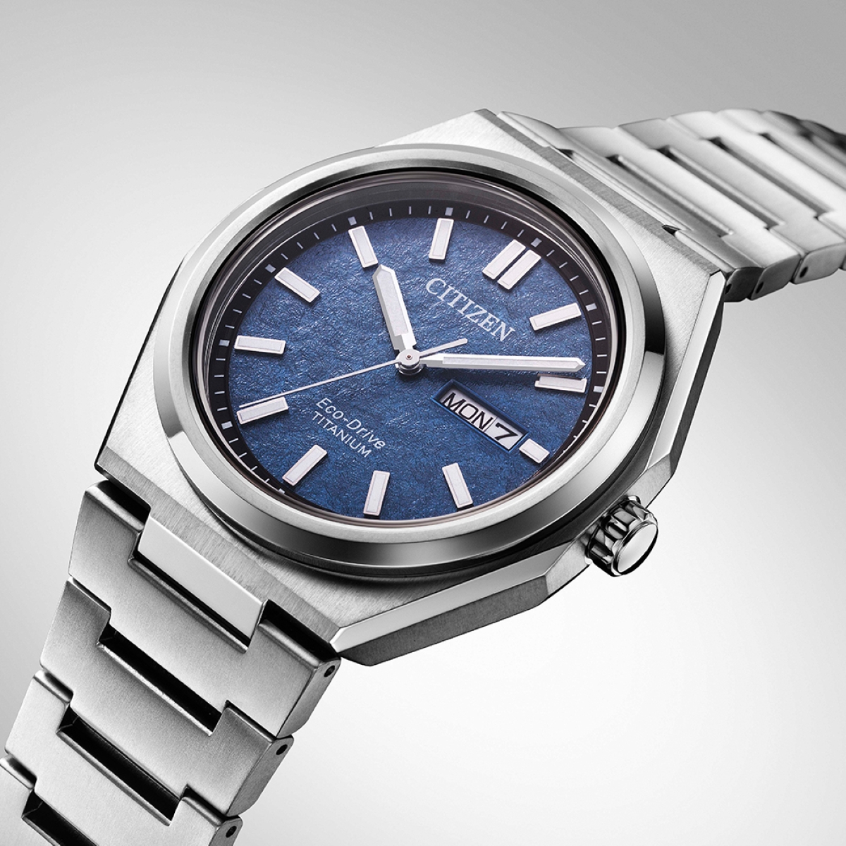 Cận cảnh đồng hồ Citizen Eco-Drive Titanium với mặt số xanh, lịch thứ và ngày tại vị trí 3 giờ, vỏ và dây Super Titanium màu bạc.