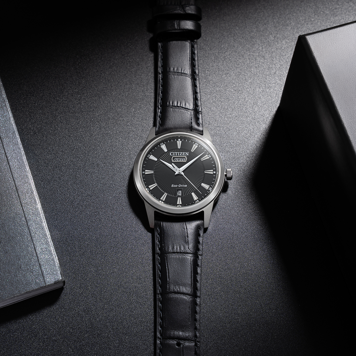 Đồng hồ Citizen Eco-Drive dây da nam mã AW0100-27e với mặt số đen, phối cùng dây da đen dập vân thanh lịch.