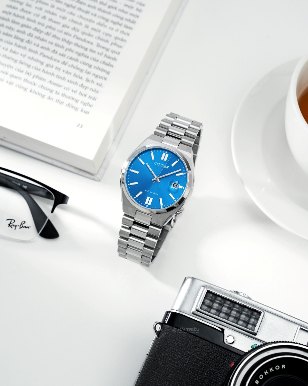 Đồng hồ nam Citizen Tsuyosa Pantone NJ0158-89L mặt số màu xanh dương đặt ở trung tâm theo góc ảnh dọc, xung quanh là các phụ kiện.
