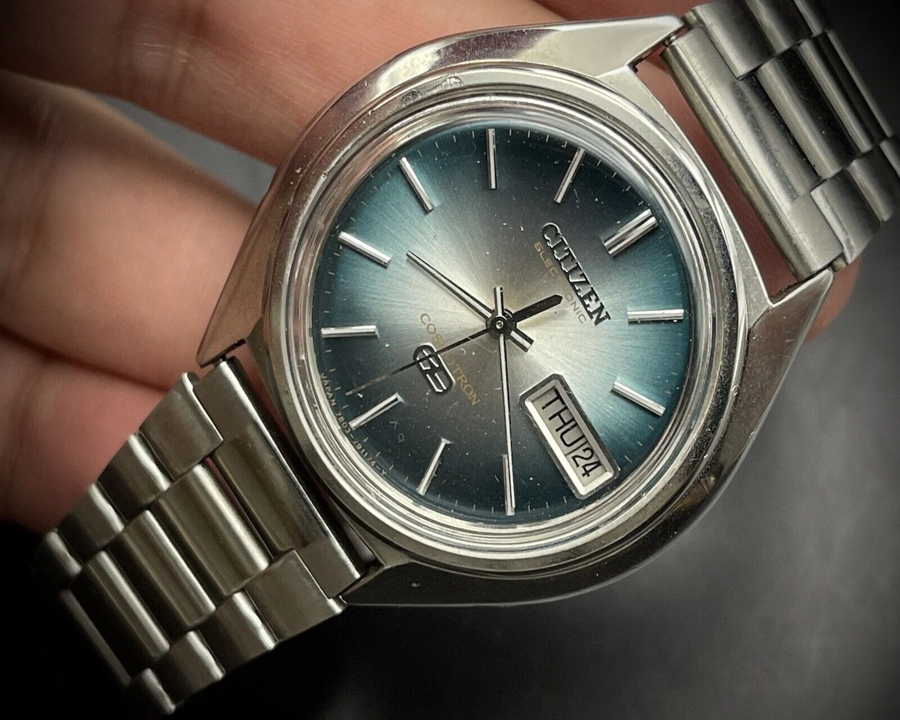 Mặt số chuyển sắc xanh dương chải tia sunburst của đồng hồ Citizen Cosmotron Electronic hiển thị lịch thứ ngày góc 4 giờ.