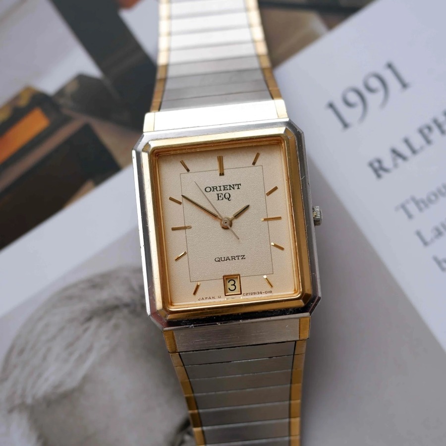 Đồng hồ cổ Orient EQ Quartz dáng chữ nhật với mặt số màu champagne, vỏ và dây kim loại đờ-mi vàng bạc.