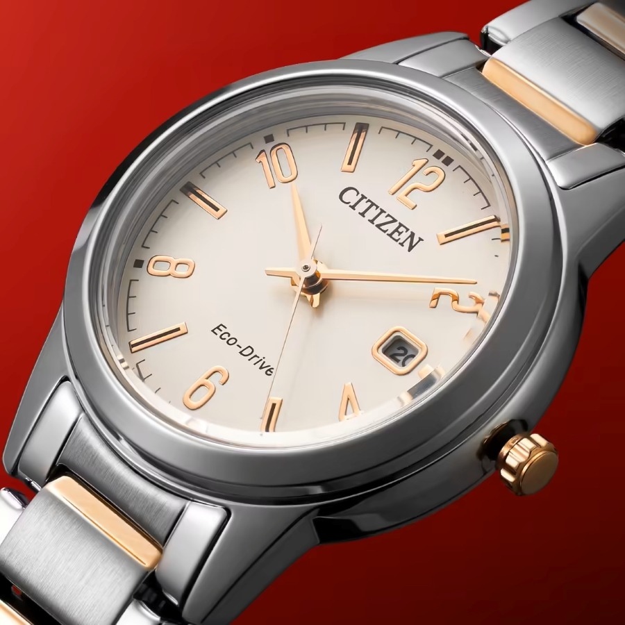 Đồng hồ Citizen Eco-Drive mặt số màu kem với kim và cọc số mạ vàng, dây thép không gỉ phối demi trên nền phông nền đỏ.