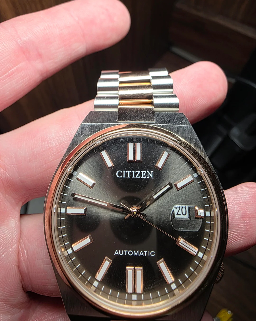 Thực tế đồng hồ Citizen Automatic trên tay người dùng với mặt kính bị phản chiếu và tạo cảm giác mờ nhòe ở góc nghiêng.